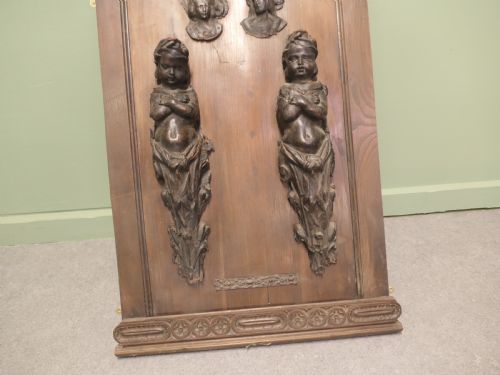 fig 1. A pair of moulded dark brown leathermache putti term figures with arms crossed, mounted vertically on a timber panel.
