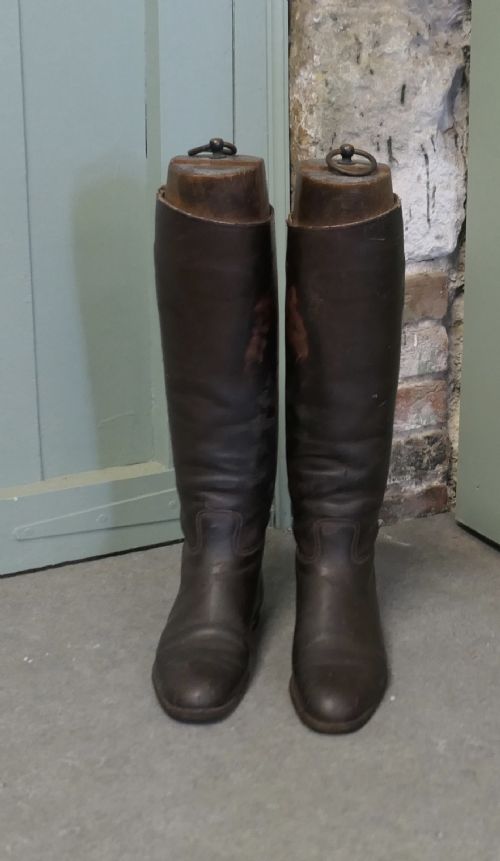 fig 1. A pair of tall dark brown leather riding boots fitted with carved wooden boot trees featuring metal pull rings.