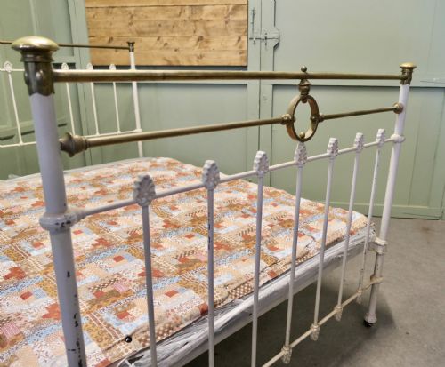 fig 1. A Victorian off-white painted cast iron double bedstead featuring brass top rails, brass finials, and a central circular motif.