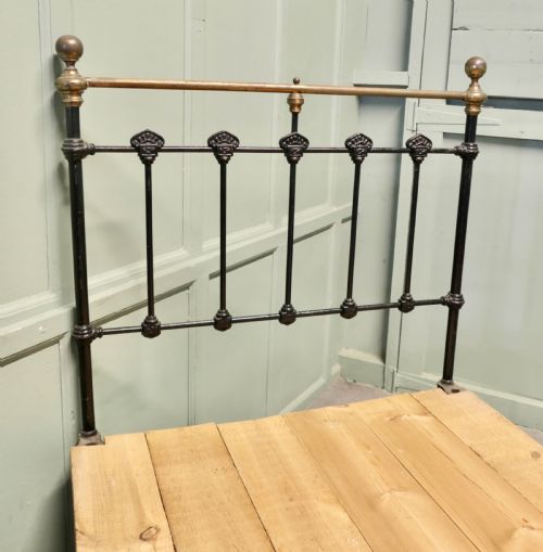 fig 1. A Victorian single bedstead featuring a black painted iron frame with vertical spindles, brass top rails, brass finials, and a wooden slate base.