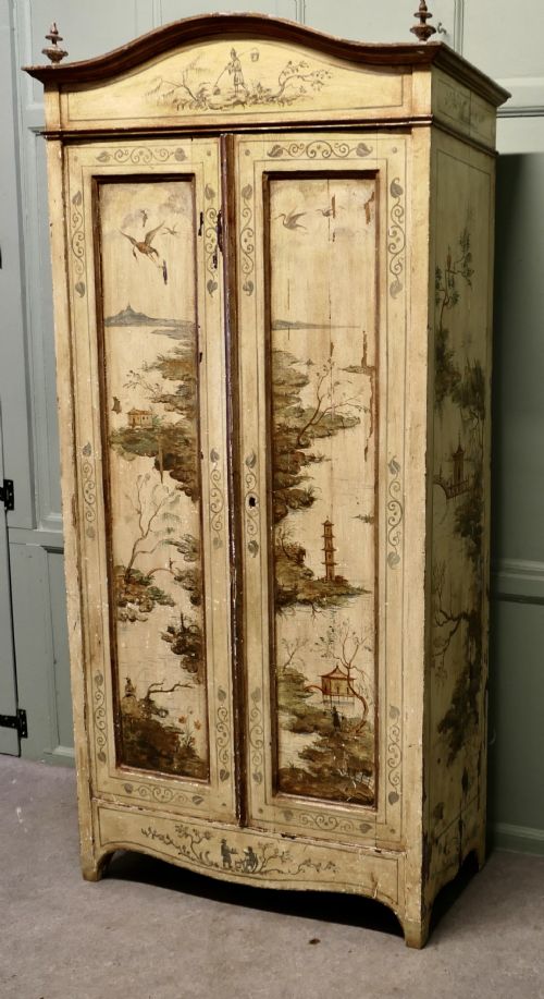 fig 1. A tall, cream-painted antique cupboard featuring hand-painted Chinoiserie landscape scenes across two full-length doors and an arched pediment.