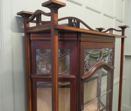 fig 1. An Art Nouveau dark mahogany display cabinet featuring leaded stained glass panels with stylized floral motifs, inlaid wood detailing, and a gallery cresting.