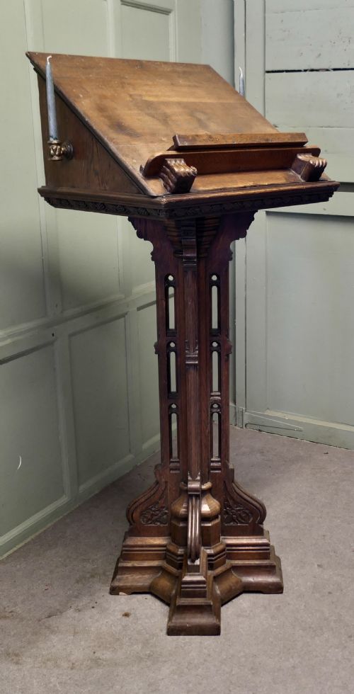 fig 1. A 19th-century carved oak reading lectern featuring a sloped book rest, candle sconces, a traceried central column, and a stepped plinth base.
