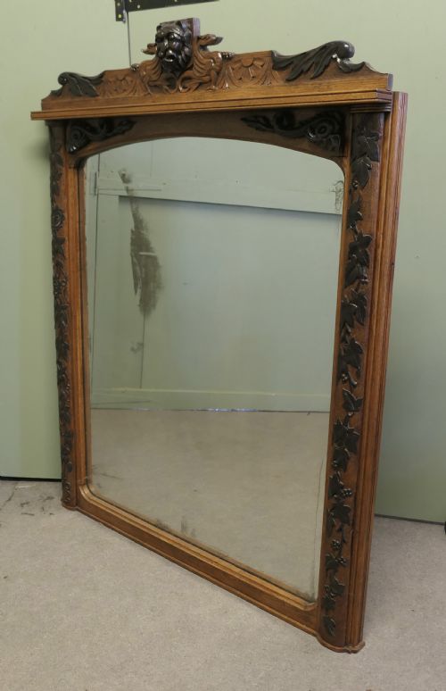 fig 1. A large rectangular oak wall mirror featuring an arched glass top, relief foliate vine side carvings, and a crest with a carved lion mask.