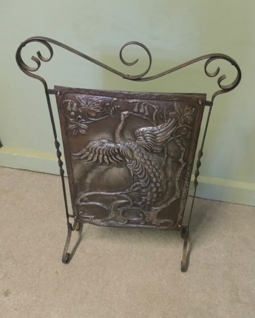 fig 1. An Arts and Crafts wrought iron fire screen featuring a central embossed metal panel with a peacock motif framed by scrolled ironwork.