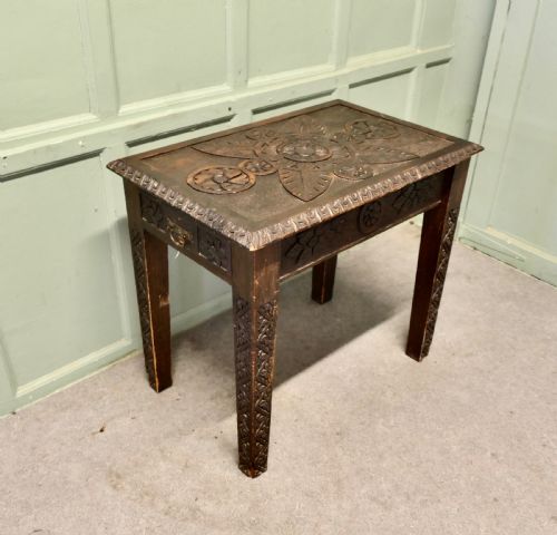 fig 1. A dark oak side table featuring carved floral motifs on the top, carved apron borders, and four carved straight legs.