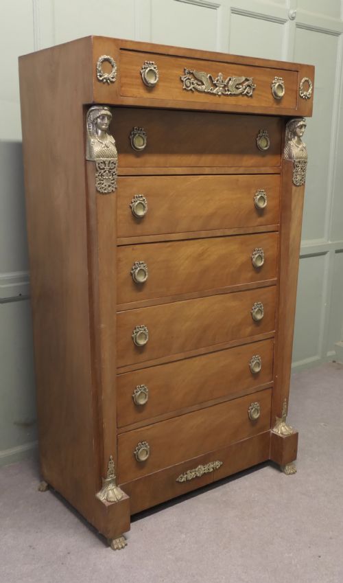 fig 1. A tall French Empire style walnut chest of drawers featuring decorative metal mounts, caryatid corner figures, swan motifs, and claw feet.