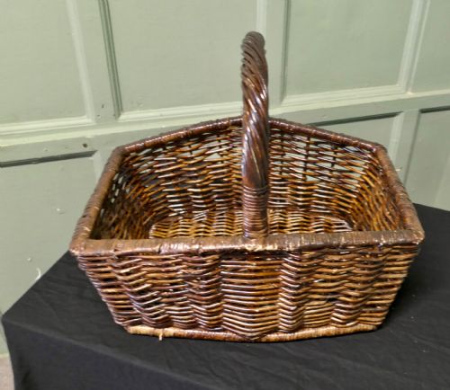 fig 1. A dark brown woven wicker basket featuring a square base, flared sides, and a high twisted arched handle.