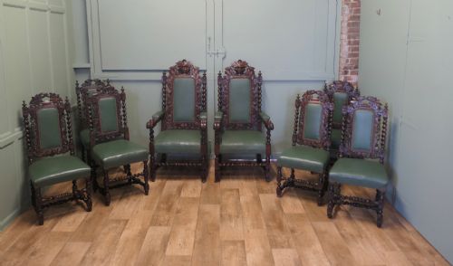 fig 1. A set of ten carved oak dining chairs featuring green leather upholstery, barley twist legs, and detailed crest rails, comprising two carver armchairs and eight side chairs.
