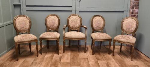 fig 1. A five-piece French Louis XVI style salon seating set featuring four side chairs and one armchair with gilded frames and floral tapestry upholstery.