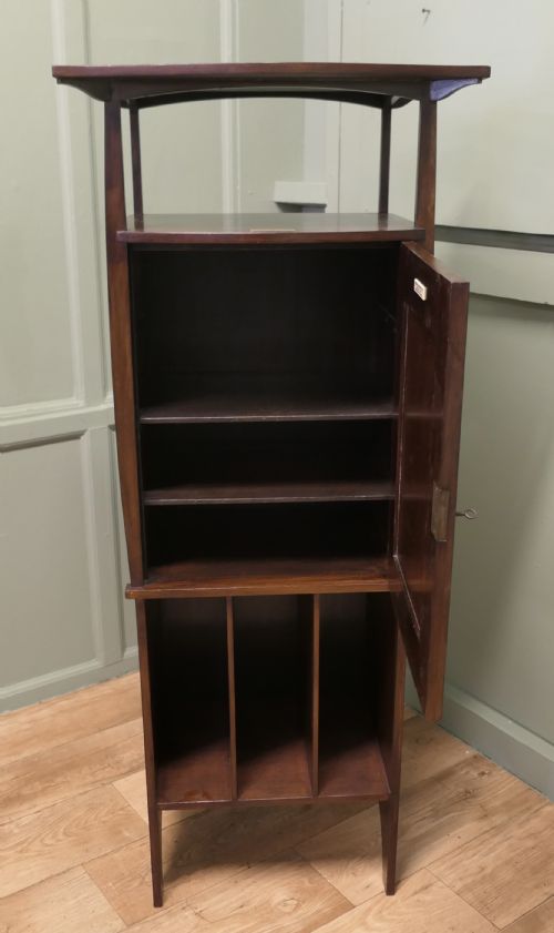 fig 1. A tall dark wood Arts and Crafts music cabinet featuring an open top shelf, a central cupboard door with inlay reading MUSIC, and three open vertical slots below.