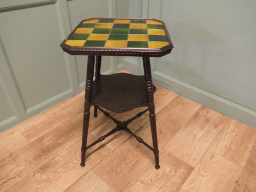 fig 1. An Arts and Crafts dark wood side table with a chequerboard top made of green and yellow glazed ceramic tiles, turned legs, and an undertier.