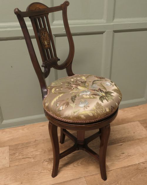 fig 1. An antique mahogany revolving music chair featuring a lyre-shaped backrest with inlaid urn motif, a round embroidered seat cushion, and four splayed legs with a central cross-stretcher.