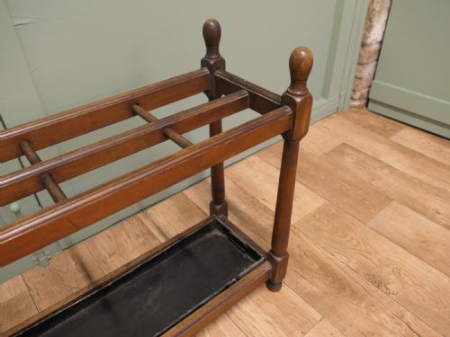 fig 2. A six-foot long Arts and Crafts wooden umbrella stand with slatted compartment dividers, turned finials, and a removable metal drip tray base.