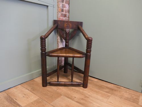 fig 1. A 19th-century dark oak turners armchair with a triangular seat, heavily turned spindle posts, three legs, and a chip-carved top backrest.