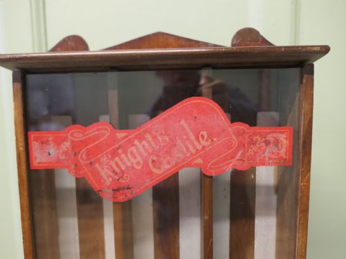 fig 1. An antique wooden countertop soap dispensing cabinet featuring glazed panels, red Knights Castile branding, and three metal lower dispensing compartments.
