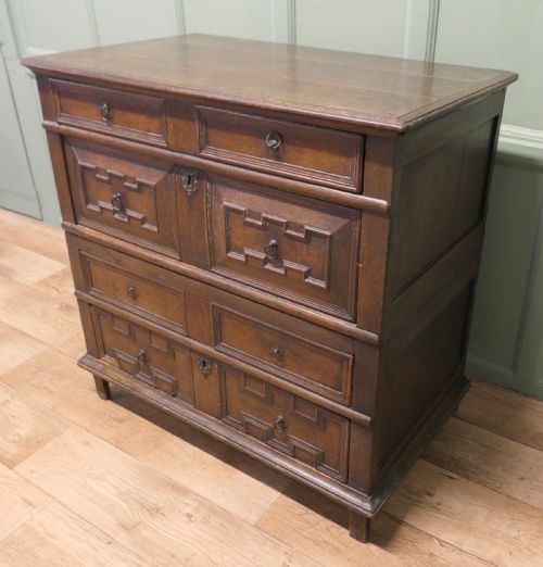 fig 1. An 18th century dark oak chest of drawers featuring geometric panelled drawer fronts, brass drop handles, and panelled sides.
