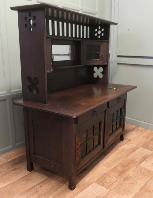 fig 1. An Arts and Crafts dark oak sideboard featuring a slatted upper gallery, central mirror, two small upper cabinets, frieze drawers, and lower cupboards with strap hinges.
