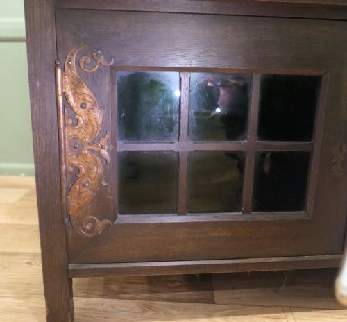 fig 2. An Arts and Crafts dark oak sideboard featuring a slatted upper gallery, central mirror, two small upper cabinets, frieze drawers, and lower cupboards with strap hinges.