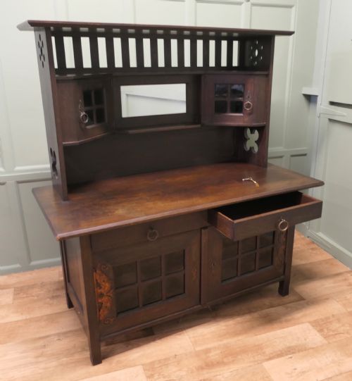 fig 3. An Arts and Crafts dark oak sideboard featuring a slatted upper gallery, central mirror, two small upper cabinets, frieze drawers, and lower cupboards with strap hinges.