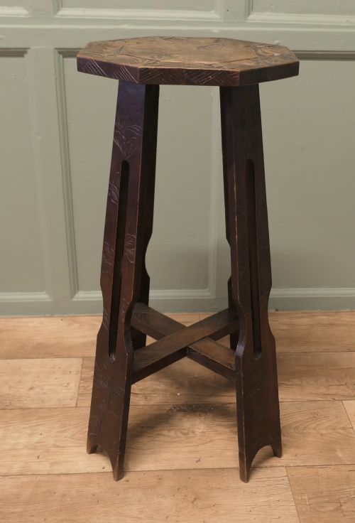 fig 2. An Arts and Crafts dark elm plant stand featuring an octagonal carved top, stylised floral carving on four pierced legs, and an X-frame stretcher.