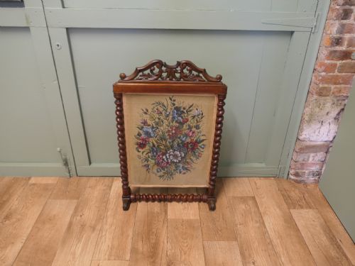 fig 1. A Victorian mahogany fire screen featuring spiral barley twist supports, an openwork carved scroll cresting, and a central needlework panel depicting a colourful floral bouquet.