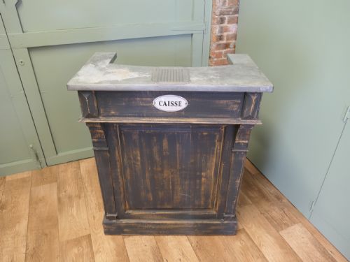 fig 1. A distressed dark charcoal painted timber greeting desk with a zinc surface and an enamel plaque inscribed with the word Caisse.