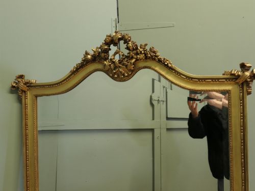 fig 1. A large arched French Rococo mirror with a gold gilt frame featuring ribbon cresting, floral garlands, and bead moulding.