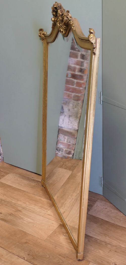 A large arched French Rococo mirror with a gold gilt frame featuring ribbon cresting, floral garlands, and bead moulding. View VII