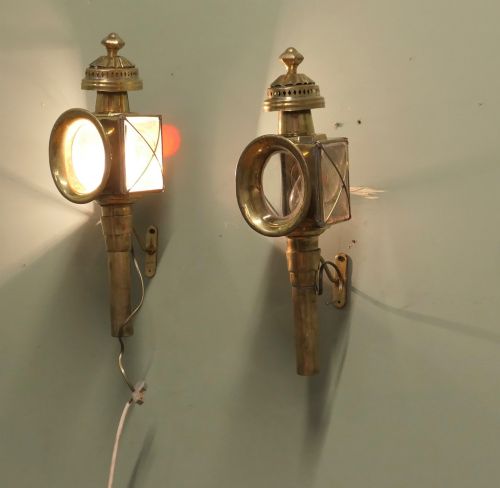 fig 1. A pair of electrified brass French carriage lanterns mounted on a wall, featuring circular front glass lenses, top finials, and tubular shafts.