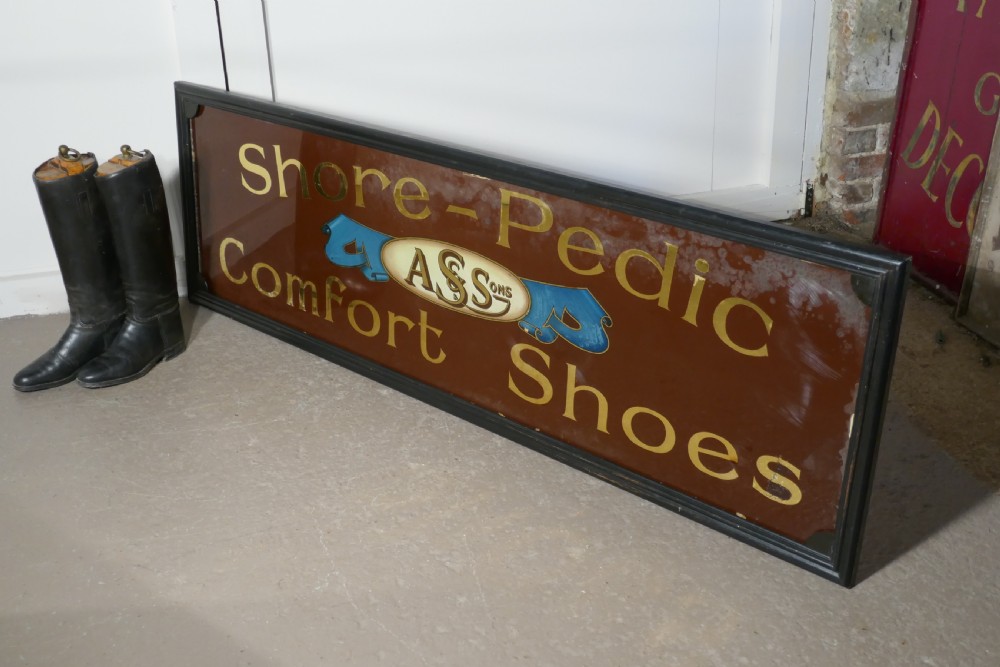 A wide rectangular black-framed commercial glass sign with gold leaf text reading Shore-Pedic Comfort Shoes on a dark brown background. View II