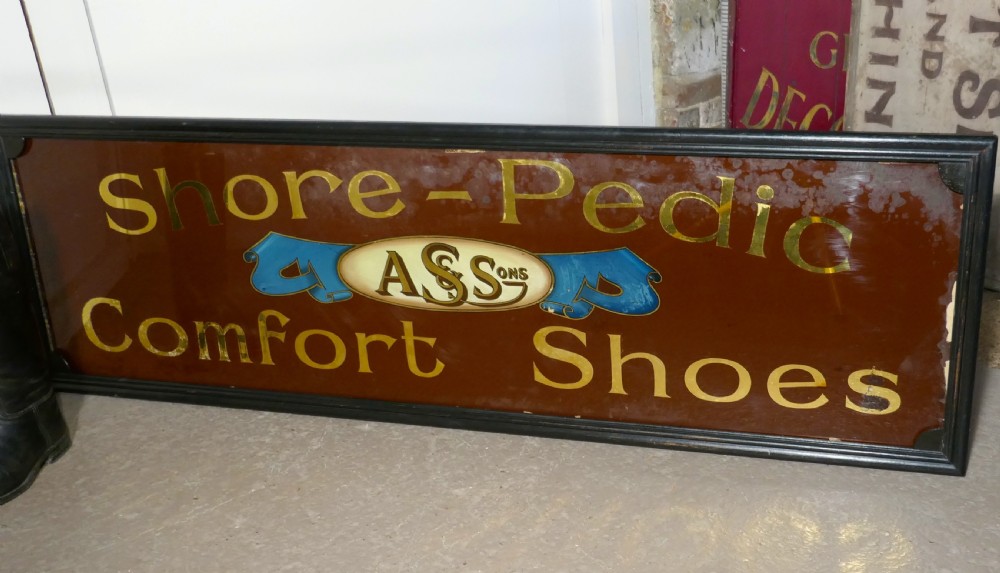 A wide rectangular black-framed commercial glass sign with gold leaf text reading Shore-Pedic Comfort Shoes on a dark brown background. View III