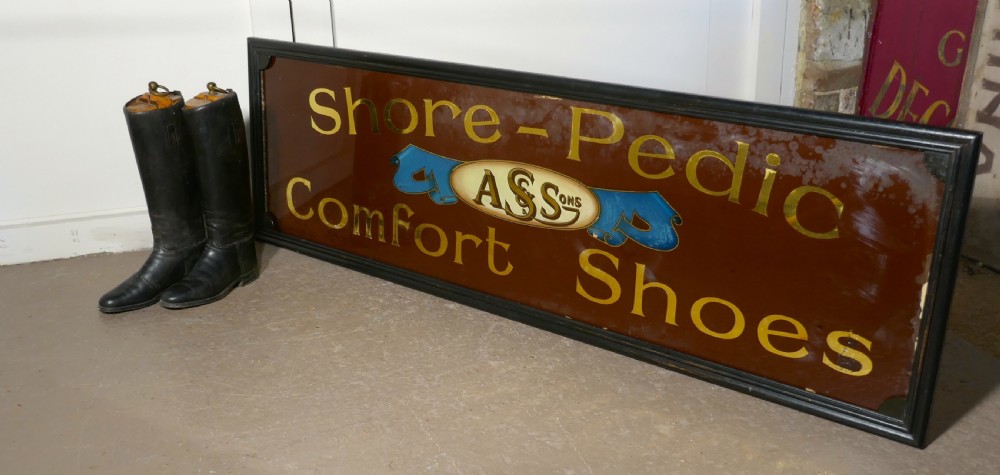 A wide rectangular black-framed commercial glass sign with gold leaf text reading Shore-Pedic Comfort Shoes on a dark brown background. View IV