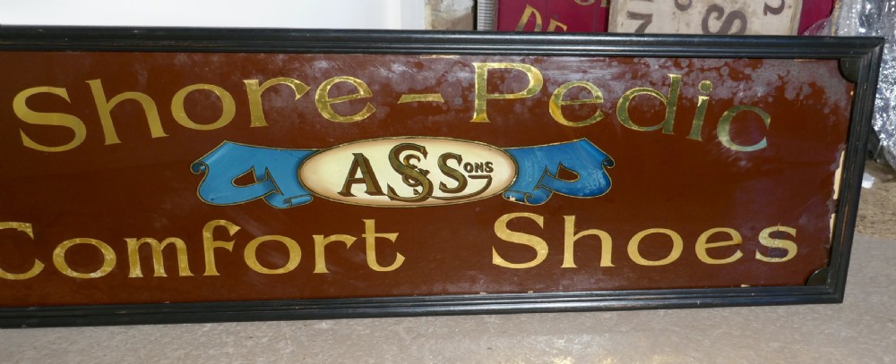 A wide rectangular black-framed commercial glass sign with gold leaf text reading Shore-Pedic Comfort Shoes on a dark brown background. View V