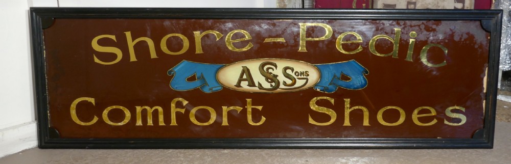 A wide rectangular black-framed commercial glass sign with gold leaf text reading Shore-Pedic Comfort Shoes on a dark brown background. View VII