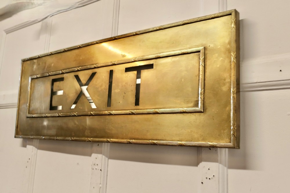 A large rectangular brass wall sign featuring stencil cut-out lettering spelling EXIT framed by textured borders. View III