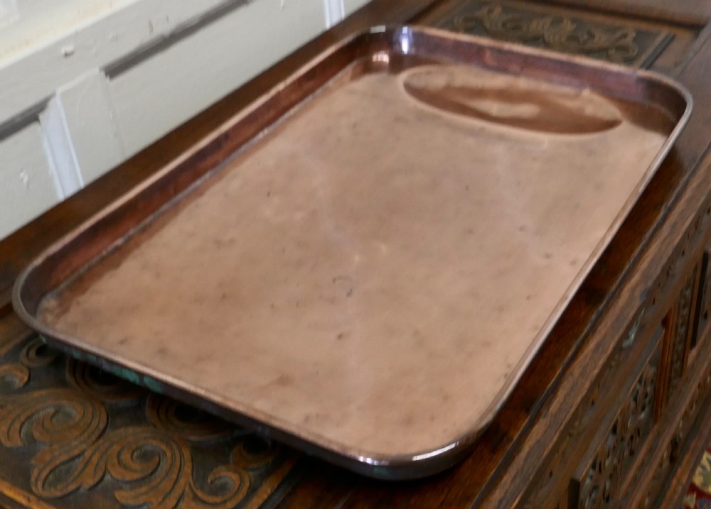 A large rectangular copper roasting tray featuring rolled rims and an indented oval gravy well at one end.