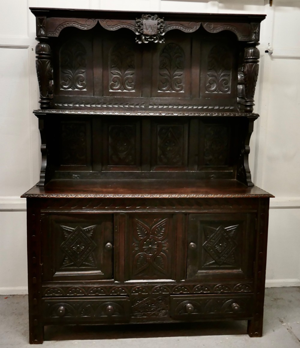 An 18th-century carved dark oak Welsh dresser featuring an upper open plate rack with carved panels above a lower cabinet base with drawers and doors.