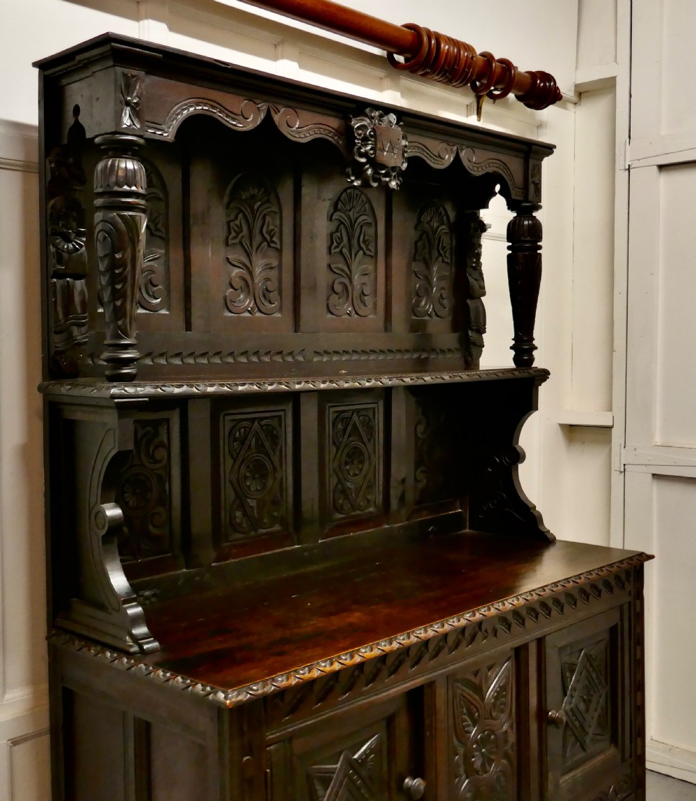 An 18th-century carved dark oak Welsh dresser featuring an upper open plate rack with carved panels above a lower cabinet base with drawers and doors. View VI