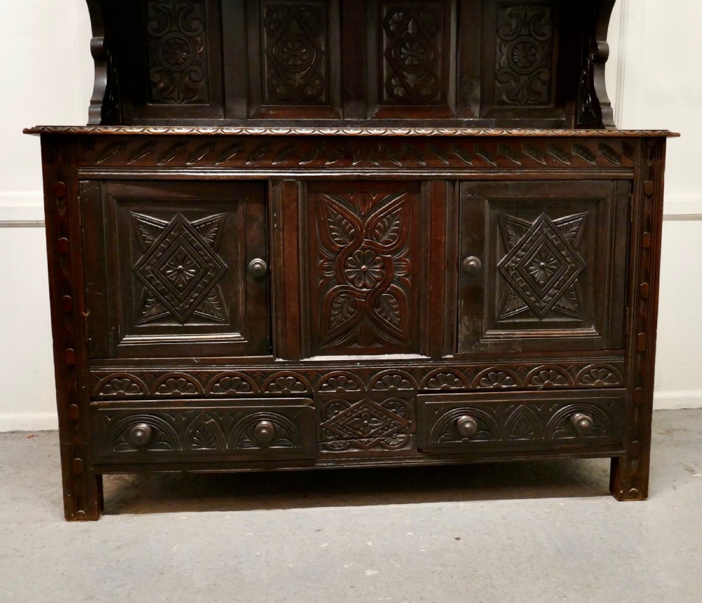An 18th-century carved dark oak Welsh dresser featuring an upper open plate rack with carved panels above a lower cabinet base with drawers and doors. View VIII