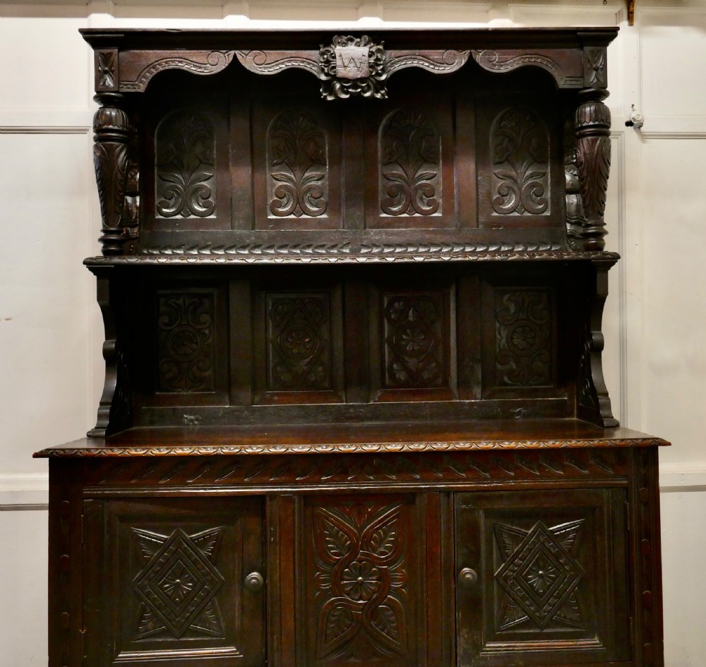 An 18th-century carved dark oak Welsh dresser featuring an upper open plate rack with carved panels above a lower cabinet base with drawers and doors. View IX