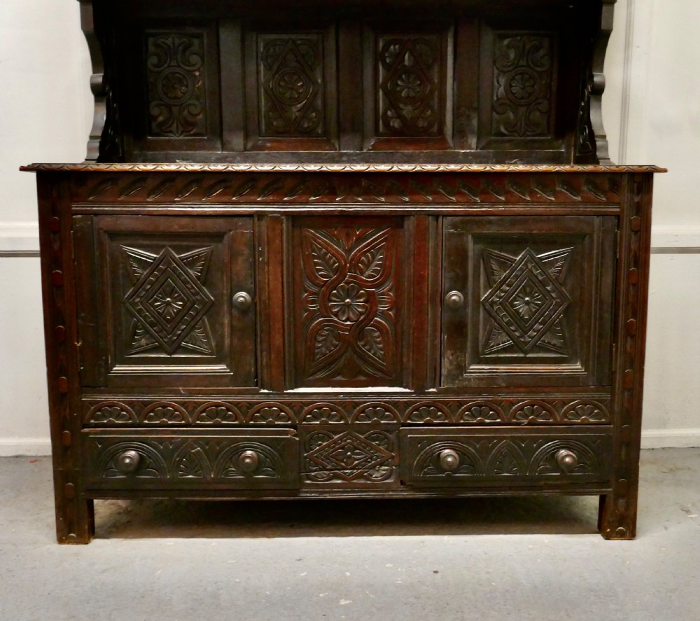 An 18th-century carved dark oak Welsh dresser featuring an upper open plate rack with carved panels above a lower cabinet base with drawers and doors. View X