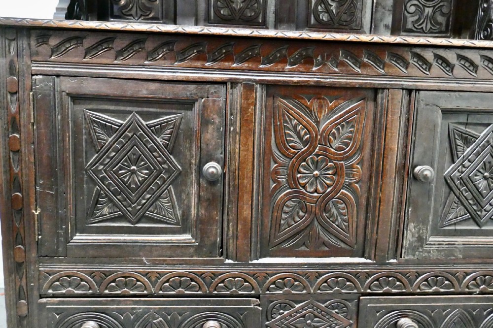 An 18th-century carved dark oak Welsh dresser featuring an upper open plate rack with carved panels above a lower cabinet base with drawers and doors. View XII