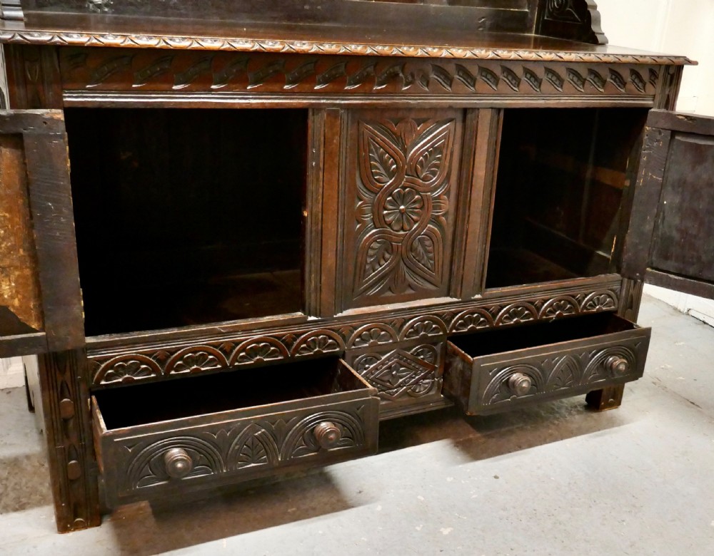 An 18th-century carved dark oak Welsh dresser featuring an upper open plate rack with carved panels above a lower cabinet base with drawers and doors. View XIII