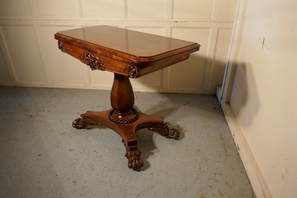 A William IV dark wood folding card table featuring a carved frieze, central turned pedestal, and a concave quadform plinth base with scroll feet. View V
