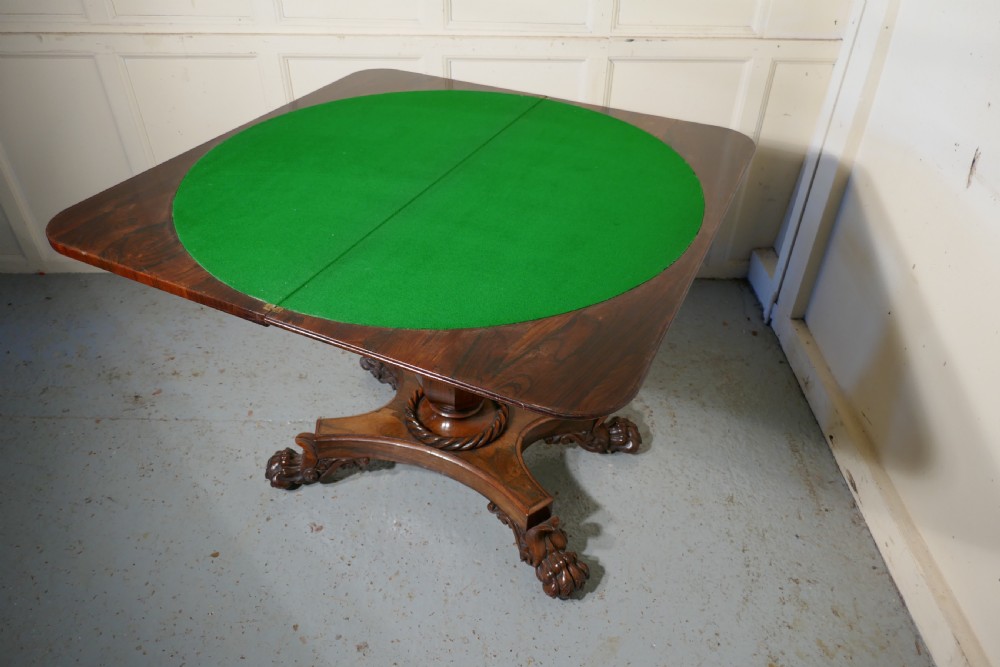 A William IV dark wood folding card table featuring a carved frieze, central turned pedestal, and a concave quadform plinth base with scroll feet. View IX
