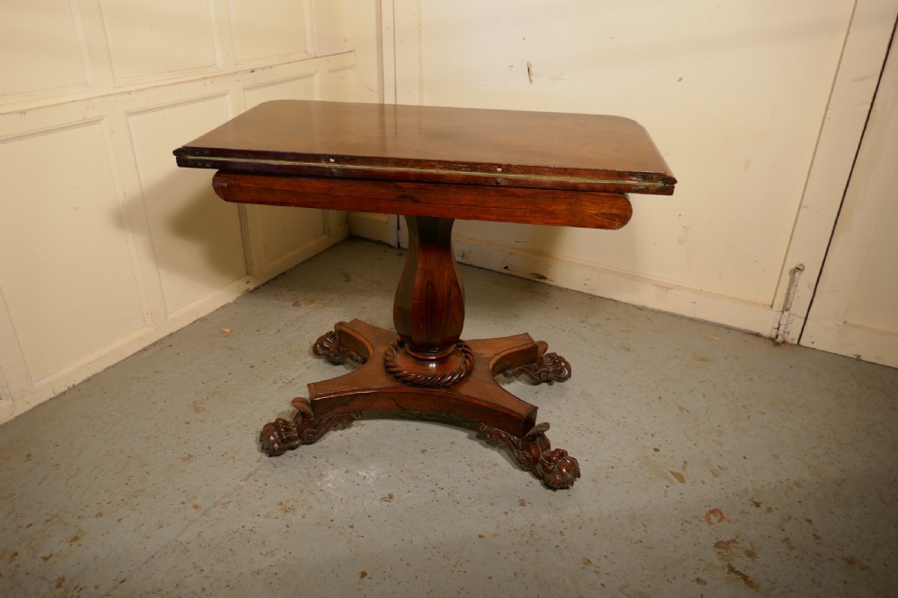 A William IV dark wood folding card table featuring a carved frieze, central turned pedestal, and a concave quadform plinth base with scroll feet. View XI