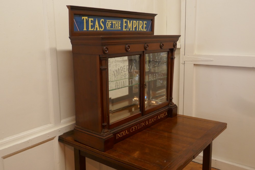 A Victorian mahogany shop counter display cabinet with etched glass doors, mirror backing, and gold lettering reading Teas of the Empire. View II