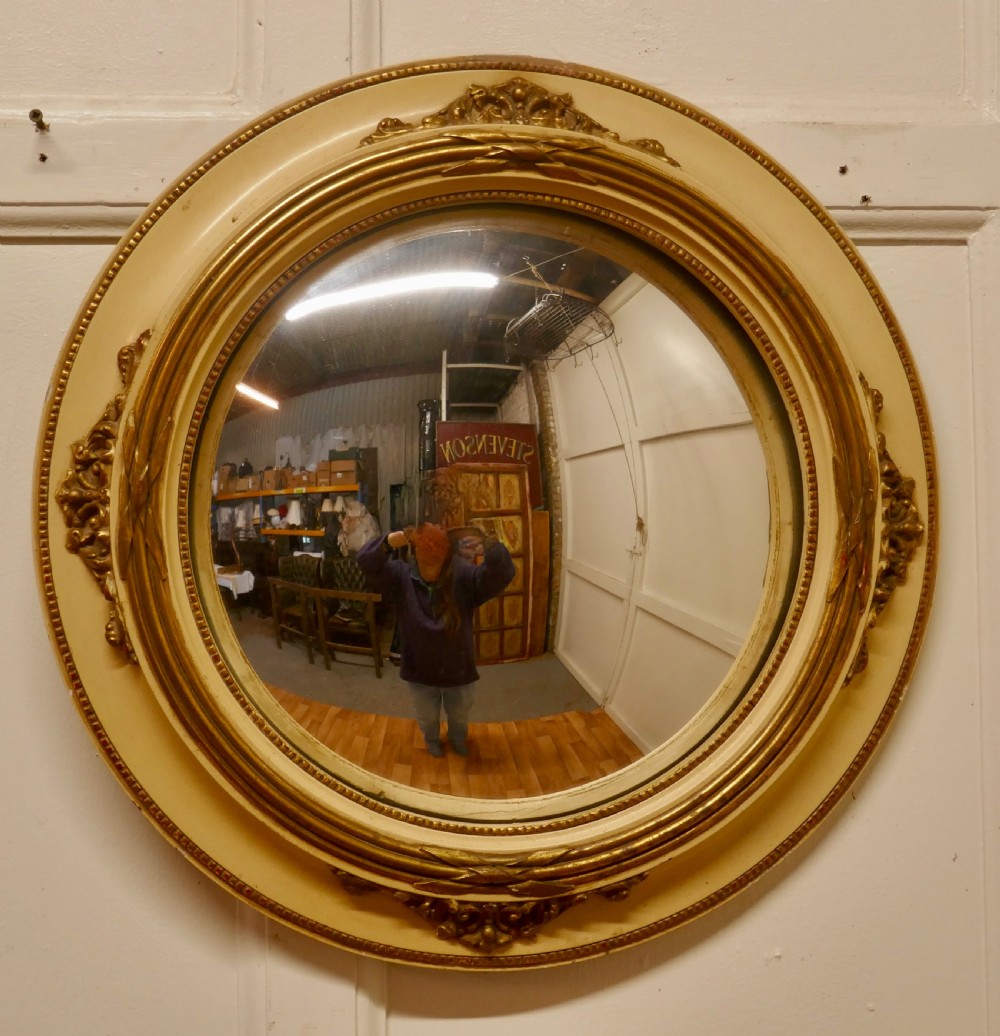 An oval French convex wall mirror featuring a painted cream frame accented with gilded acanthus leaf embellishments. View II