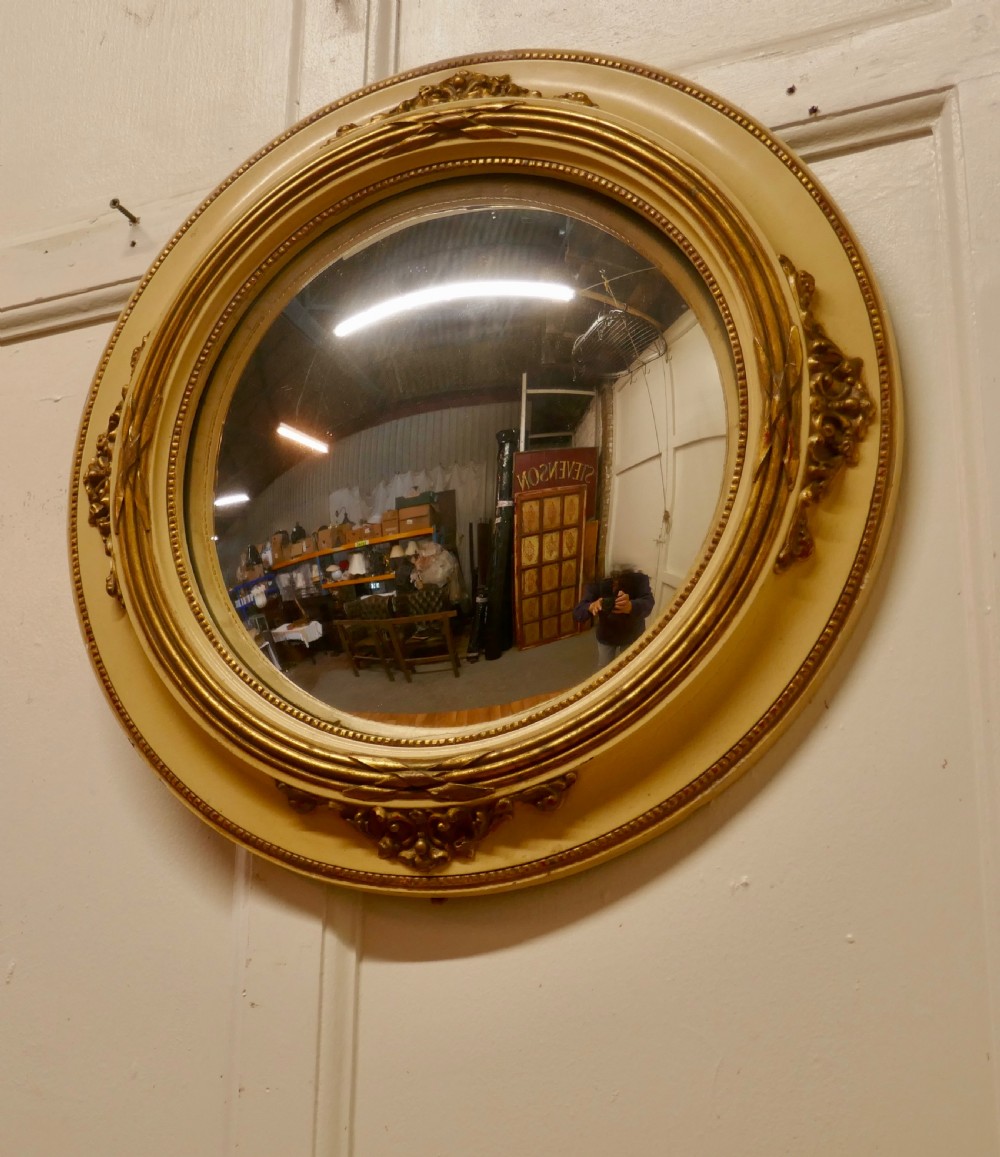 An oval French convex wall mirror featuring a painted cream frame accented with gilded acanthus leaf embellishments. View III